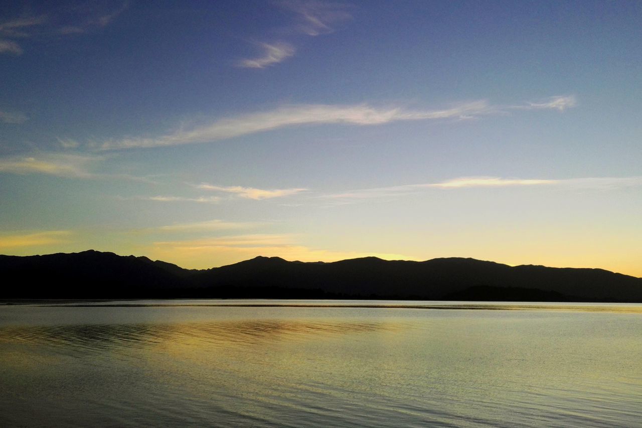 SCENIC VIEW OF SEA BY SILHOUETTE MOUNTAINS AGAINST SKY