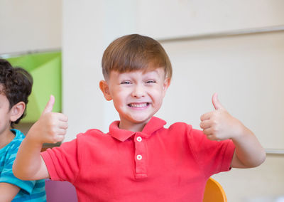 Portrait of smiling boy gesturing thumbs up sign in classroom