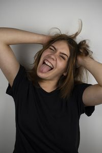 Laughing young woman making face wile standing against gray background
