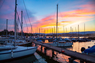 Sailboats moored in harbor at sunset