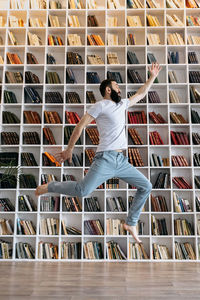 A brutal man with a beard jumping up in the library among the bookshelves
