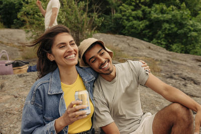 Happy woman holding drink can sitting with arm around male friend
