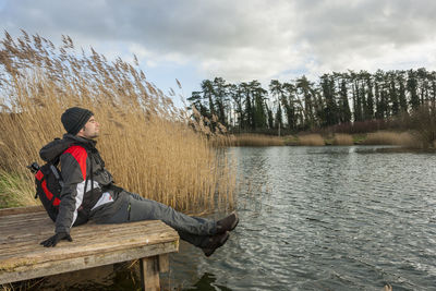 Man sitting by lake against sky