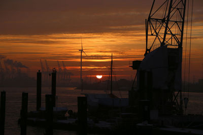Silhouette sailboats on pier by sea against orange sky