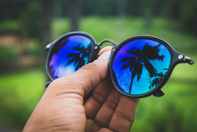 Close-up of hand holding sunglasses against trees