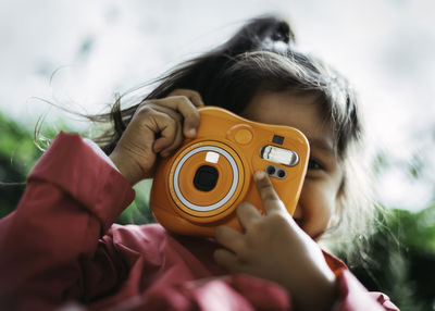 Cute little girl snapping a photo with an instax orange camera.