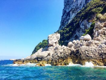 Scenic view of wave splashing on rocks against clear sky