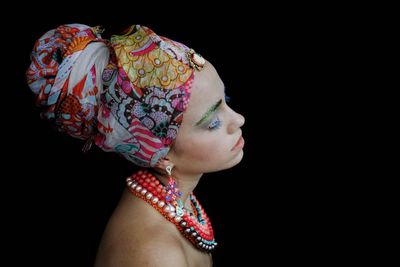 Close-up of young woman wearing headscarf against black background