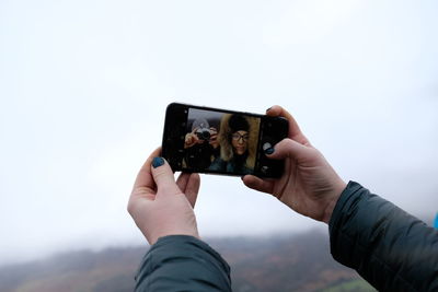 Man photographing with mobile phone against sky