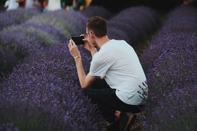 Man crouching while photographing purple lavender flowers on field