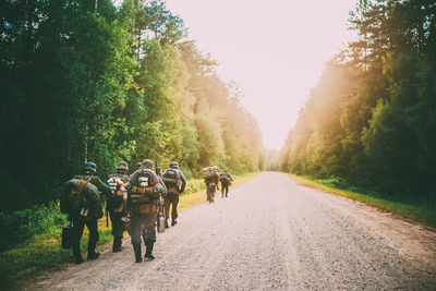 Rear view of people walking on road along trees