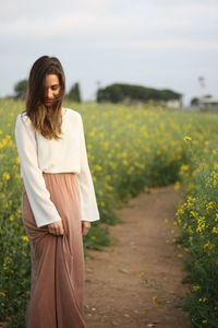 Young woman standing by flowering plants against sky
