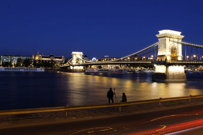 Illuminated bridge over river with city in background