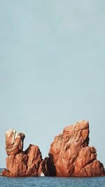 Rock formations by sea against clear sky