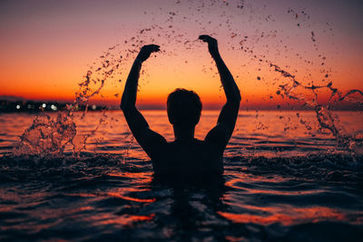 Silhouette man splashing water in sea against clear sky during sunset