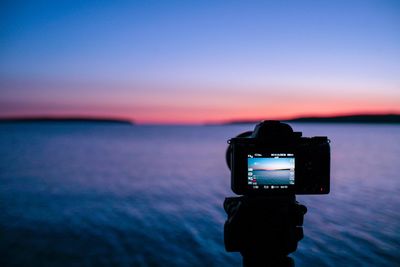 Reflection of camera on sea against sky during sunset