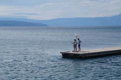 People standing on pier amidst sea against sky