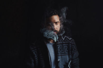 Portrait of young man smoking over black background