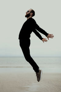 Side view of man jumping at beach against sky