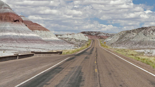 Road surrounded by mountains against cloudy sky