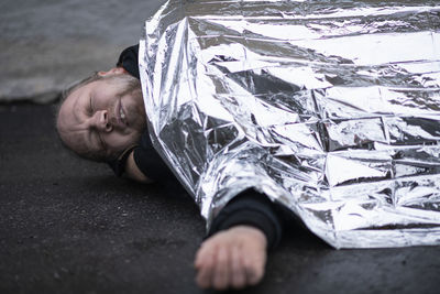 Unconscious man in medical shock lying under emergency blanket