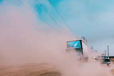 Vehicles on dirt road against sky