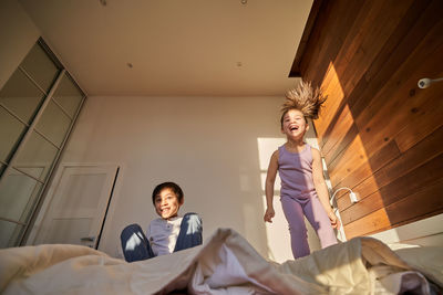 An asian boy and a girl in a purple suit are merrily jumping on the bed.