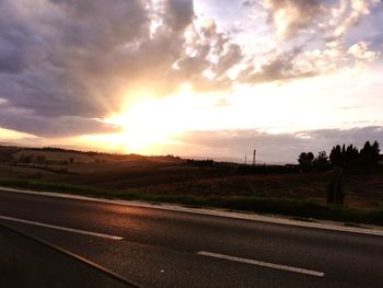 Road by field against sky during sunset