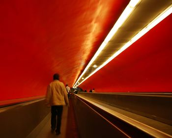 Rear view of man walking on illuminated escalator