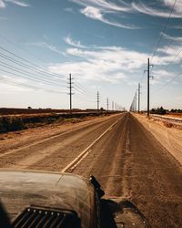 Road by electricity pylon against sky