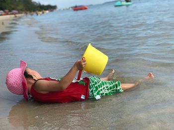 Girl holding bucket while lying at beach