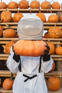 Person wearing spacesuit while holding pumpkin in store