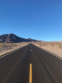 Road leading towards desert against clear blue sky