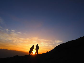 Silhouette men standing on mountain against sky during sunset