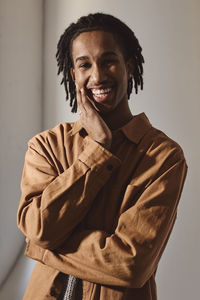 Portrait of smiling young man with hand on chin against wall