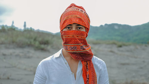 Portrait of man wearing scarf standing on field against sky