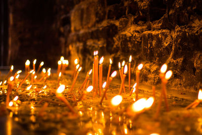 Close-up of burning candles by wall at night