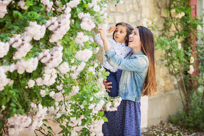 Mother and little handsome baby boy looking at bush with white roses