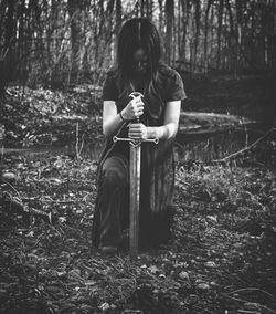 Woman holding sword while kneeling in forest