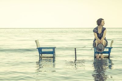 Full length of woman sitting on seat against seascape