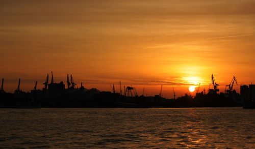 Silhouette commercial dock by sea against sky during sunset