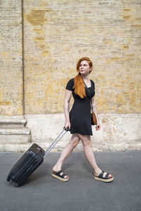 Casual woman with suitcase walking on city street