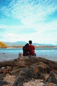 Rear view of couple sitting on driftwood at beach