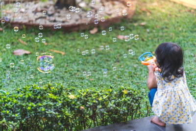 Little asian girl playing with soap bubbles in garden.