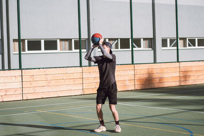Blond boy in sportswear practices shooting a basketball from behind the three-point line. outdoor 