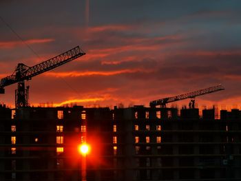 Silhouette cranes at construction site against sky during sunset