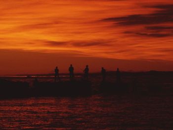 Silhouette people on beach against sky during sunset