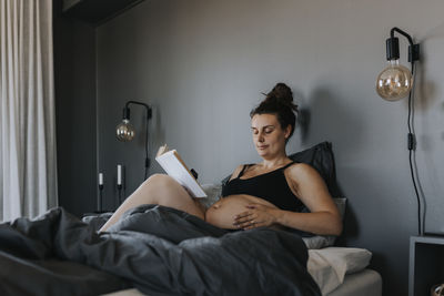 Pregnant woman relaxing in bed and reading book