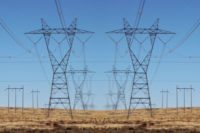 Low angle view of electricity pylon on field against clear blue sky