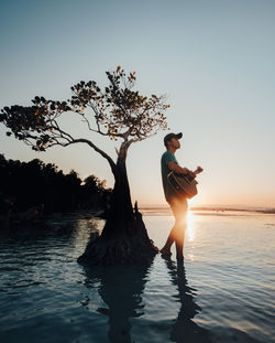 Side view of woman with arms outstretched standing on beach against sky